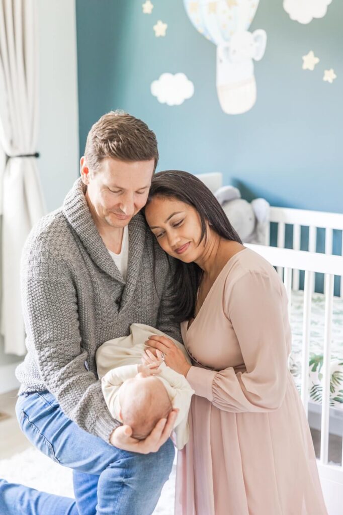 A family at home in Marin, California smile down at their newborn baby by the crib