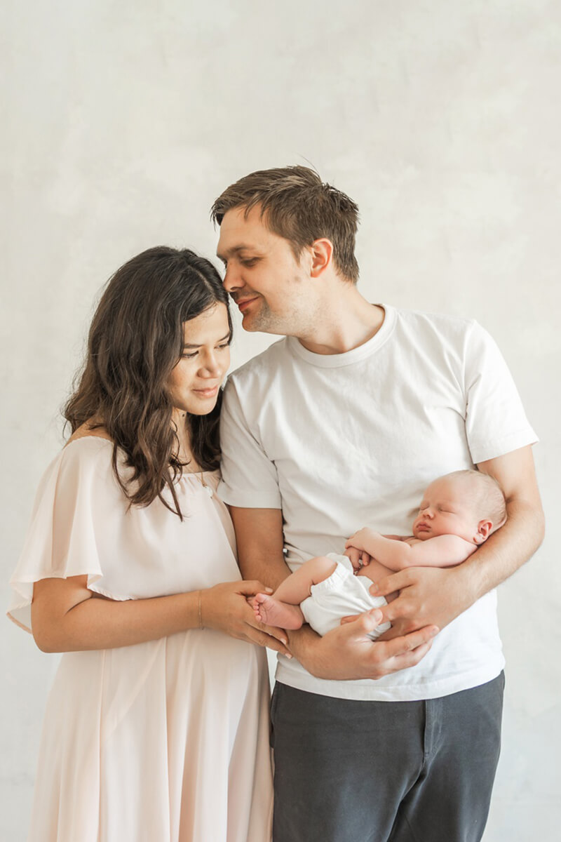 dad holding baby kissing mom at a Bay Area newborn studio