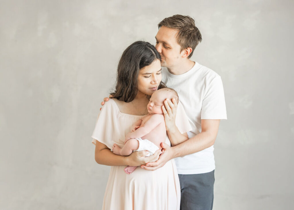 dad kissing moms head while mom is kissing baby in a Bay Area photography studio